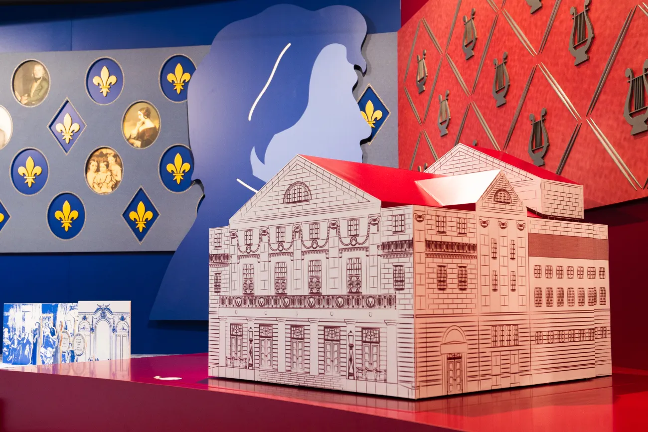 Detailansicht: Modell des Hof-Theaters. Im Hintergrund eine Wand mit historischen Porträts sowie musikalischen Dekorationen.