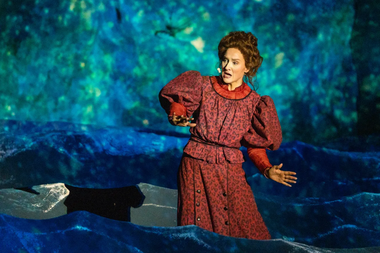 Szene: Frau in rotem Kleid mit Puffärmeln und hochgesteckten Haaren singt inmitten der Wellen