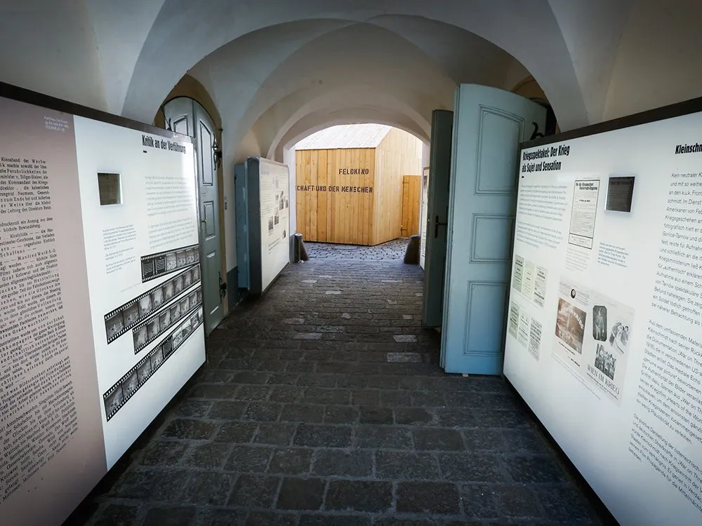 Gewölbter Gang mit Kopfsteinpflaster zu Holzbau. Infotafeln mit Texten und Filmstreifen