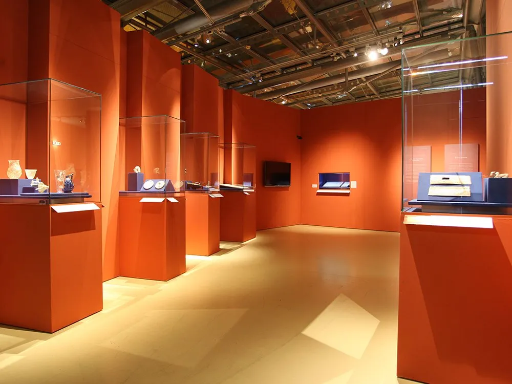 Ausstellungsraum: Vitrinen mit historischen Artefakten, orangene Wände