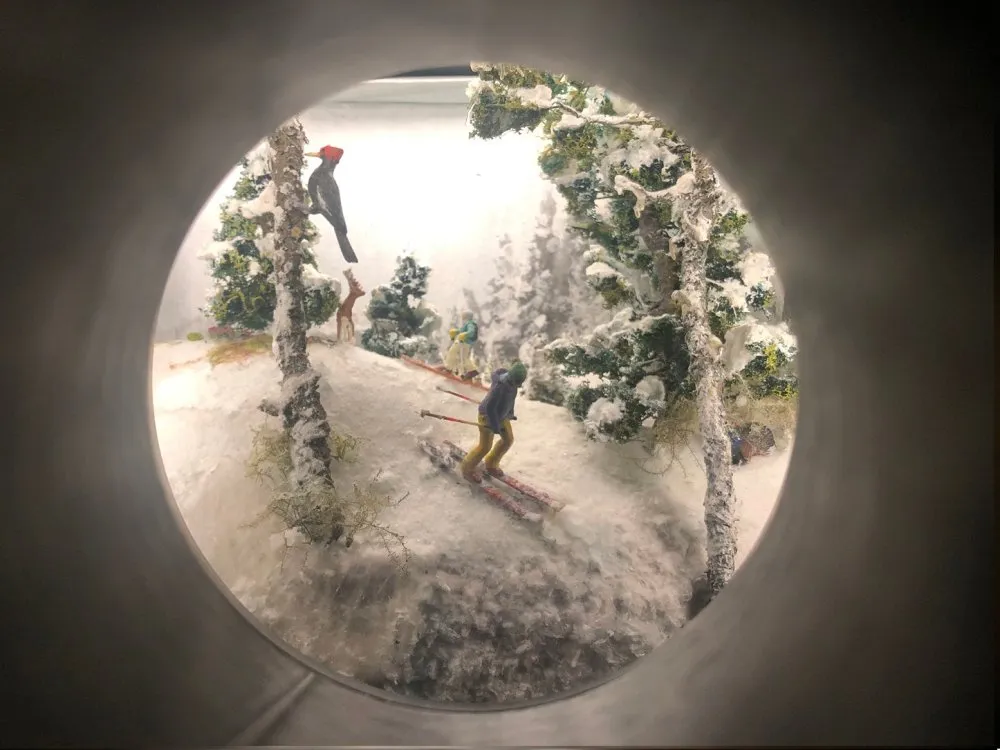 Mini-Diorama mit schneebedeckten Bäumen, einem Skifahrer, einer Eule, einem Reh und weiteren Figuren in einer winterlichen Landschaft.