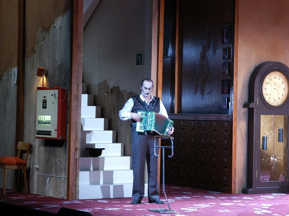 Szene: Mann steht vor Treppe mit Akkordion