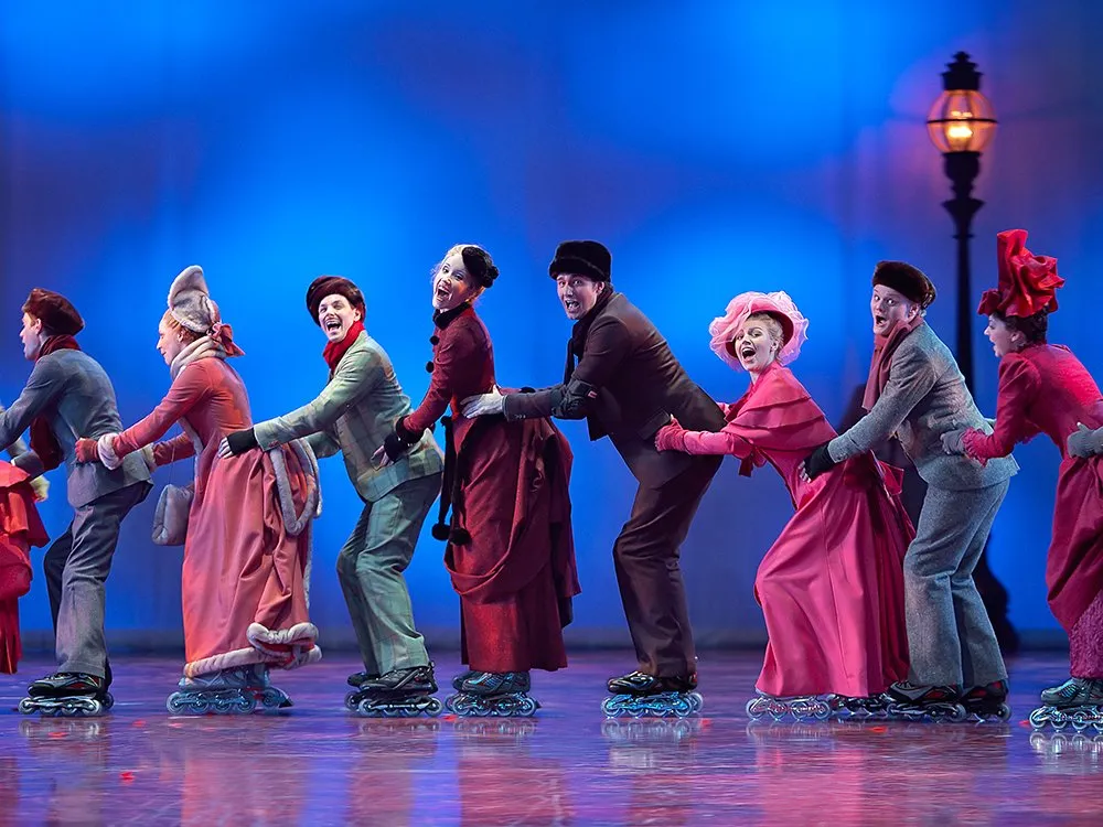 Szene: Personengruppe in bunten historischen Kostümen, die auf Rollschuhen eine Kette bilden