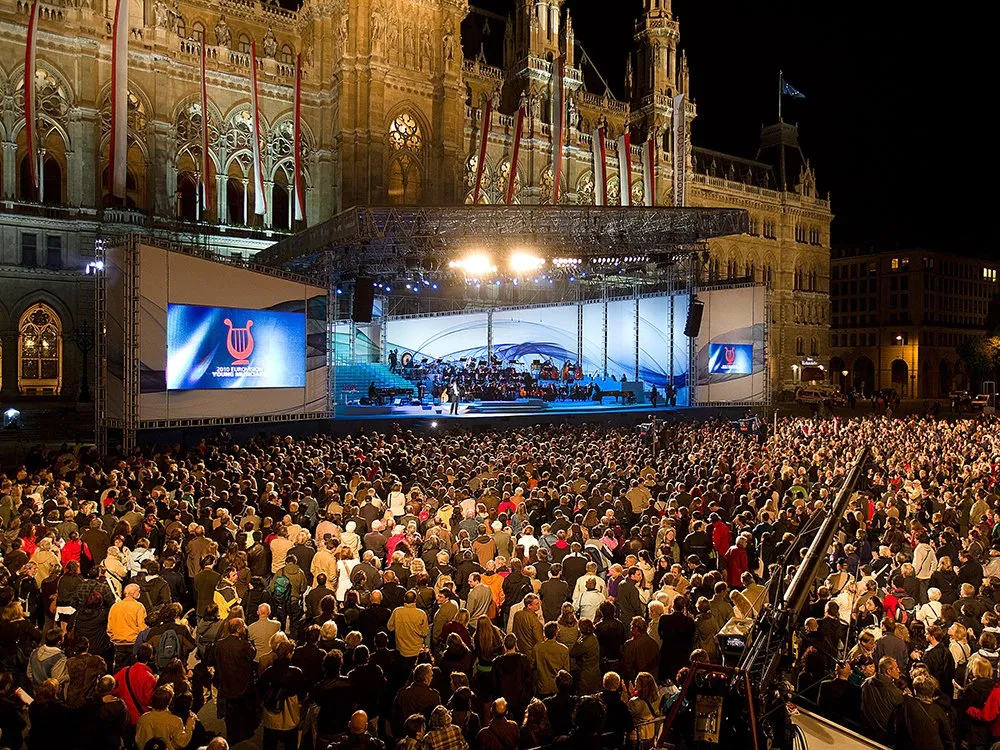 große Menschenmenge vor einer beleuchteten Bühne mit Orchester