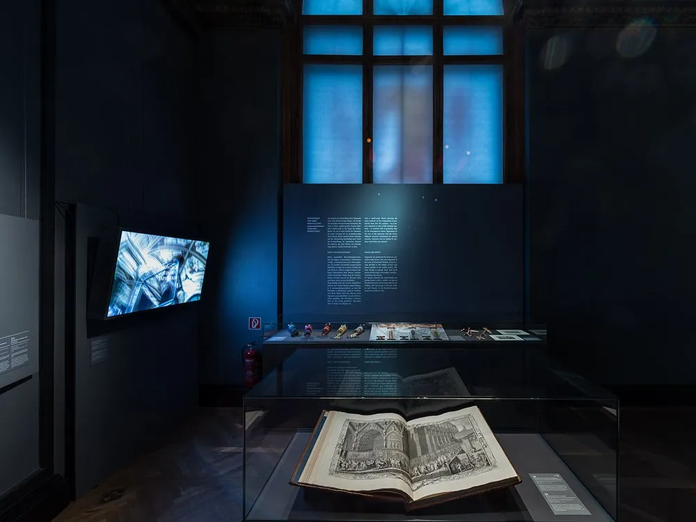 Vitrine mit offenem Buch, Bildschirm und andere Artefakte im Hintergrund