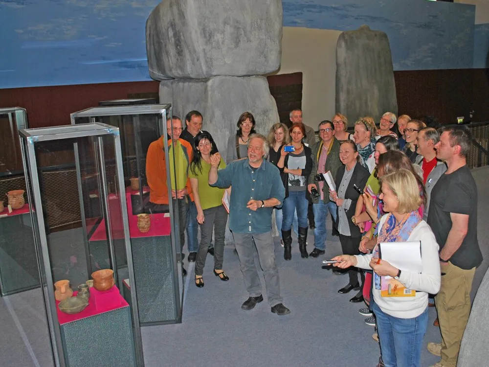 Gruppe um einen Guide vor Vitrinen mit Töpfen, umgeben von Steinformationen im Museum.