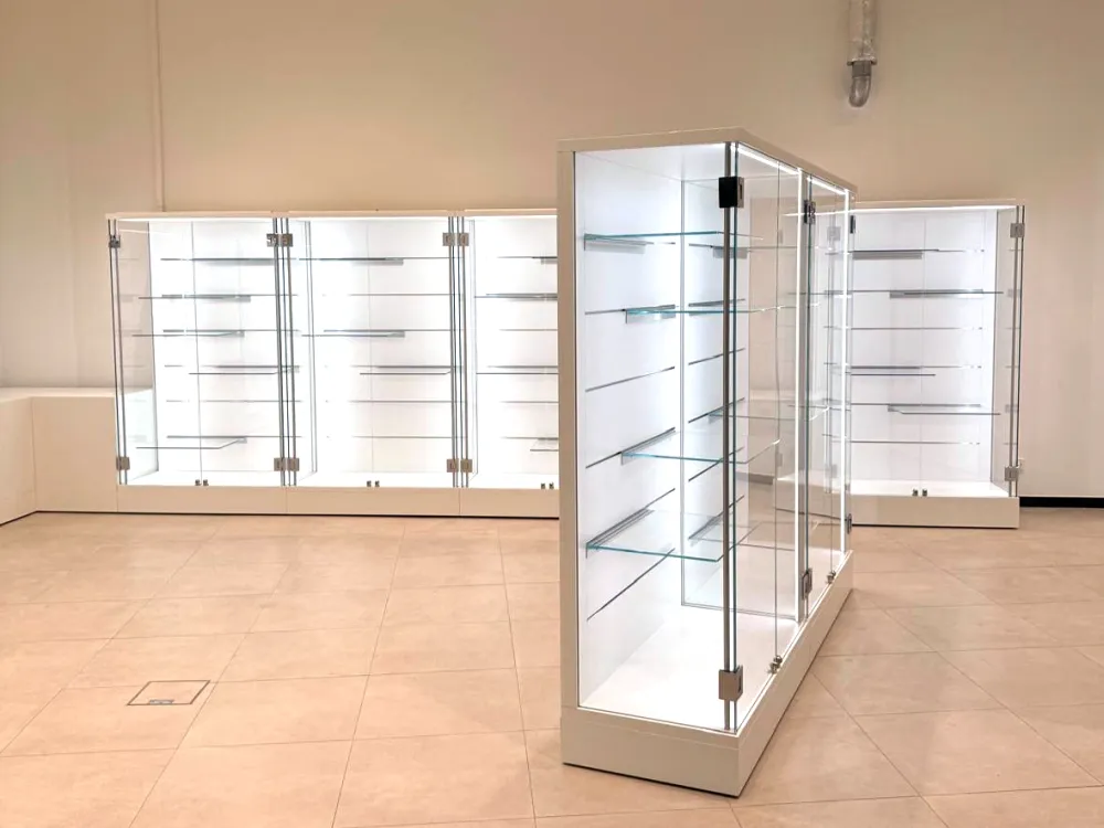 Eine Reihe moderner, weißer Vitrinen mit Glasregalen, teilweise an der Wand und eine frei im Raum stehend.