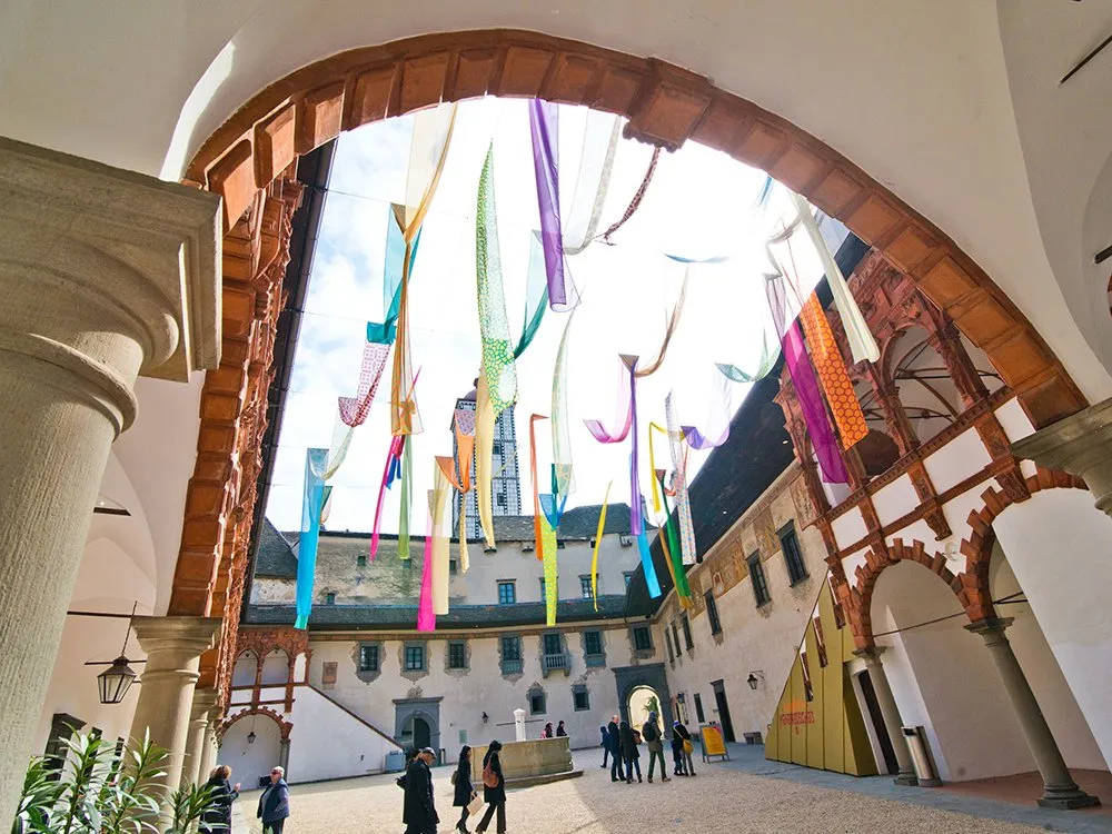 Innenhof verziert mit bunten Stoffbahnen, die von einem Bogen hängen, und Besuchern