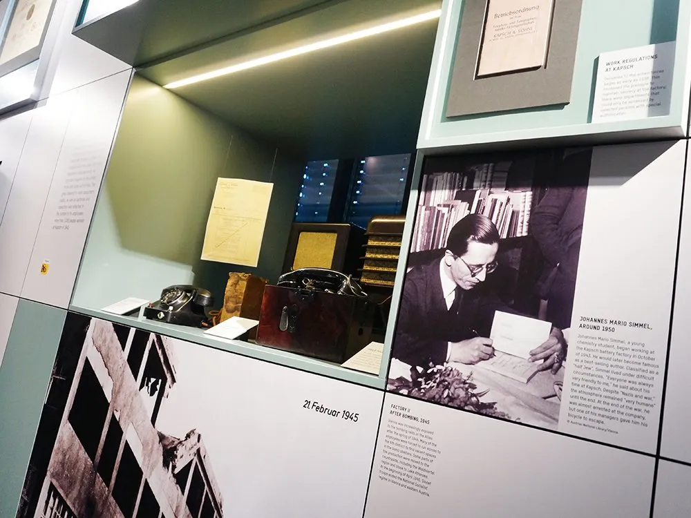 usstellungsraum mit altem Telefon, Dokumenten, einem Foto von Johannes Mario Simmel und einem Bild einer zerstörten Fabrik