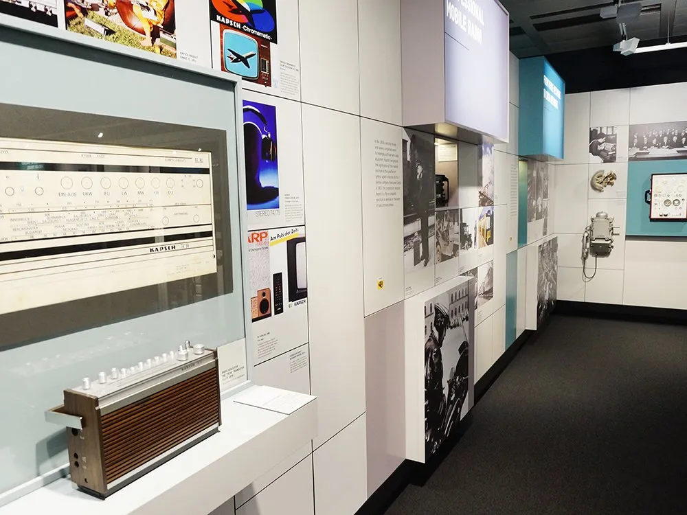 Ausstellungsraum mit einem historischen Radio und einem Schaukasten mit alten Dokumenten, umgeben von Fotos und Plakaten