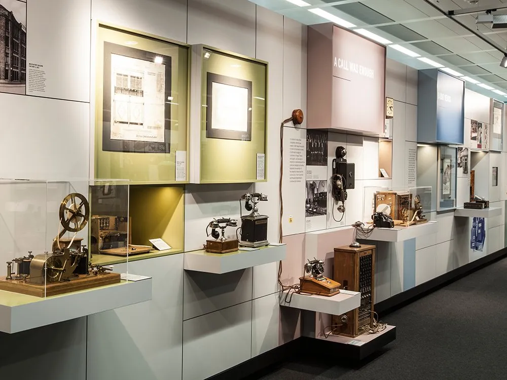Ausstellungsraum mit historischen Kommunikationsgeräten wie alten Telefonen und einem Morsegerät, sowie Fotos und Dokumenten an den Wänden