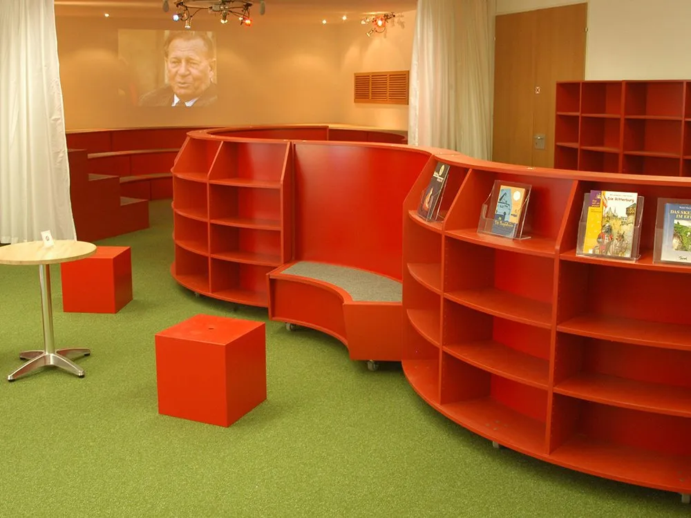 Wabenförmige rote Bücherregale mit Büchern, rote Sitzwürfel, Tische