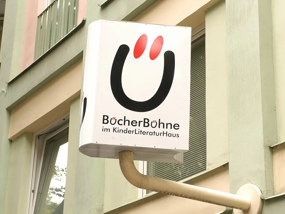 Schild mit dem Logo "BücherBühne im KinderLiteraturHaus" an einer Gebäudefassade