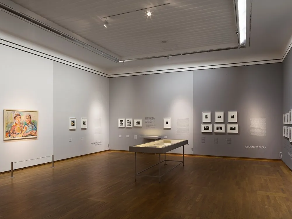 Ausstellungsraum: Wände in Grauabstufungen mit Gemälden, Vitrinentisch im Raum