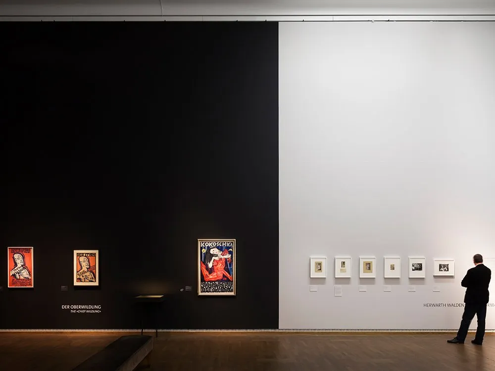 Ausstellungsraum: hohe Wand, eine hälfte schwarz, andere weiß, mit Gemälden