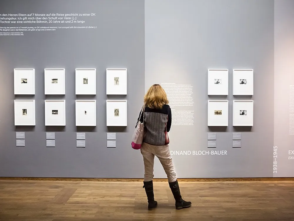 Frau steht vor grauer Wand und betrachtet Bilder