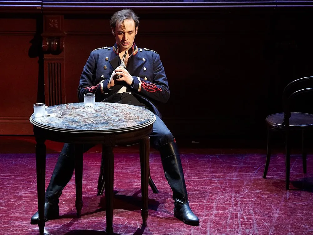 Mann in Uniform sitzt an einem runden Tisch mit Gläsern, hat Pistole auf sich gerichtet