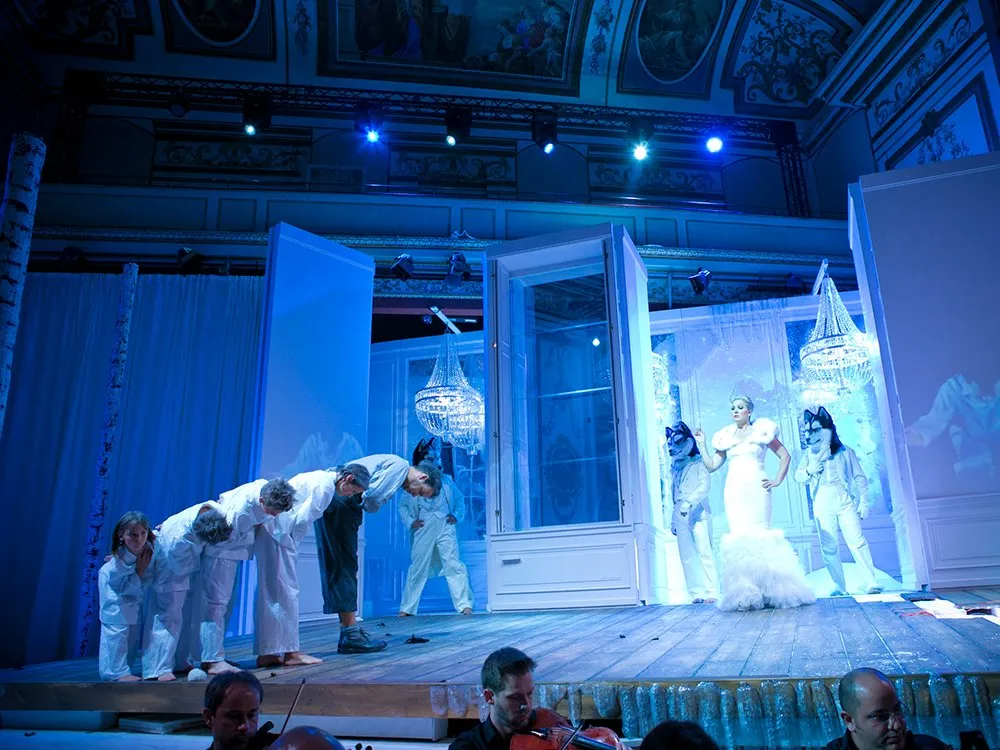 Szene: Darsteller in weißen Gewändern verbeugen sich vor Schneekönigin in weißen Kleid, Zwei Personen in Wolfkostüm neben ihr