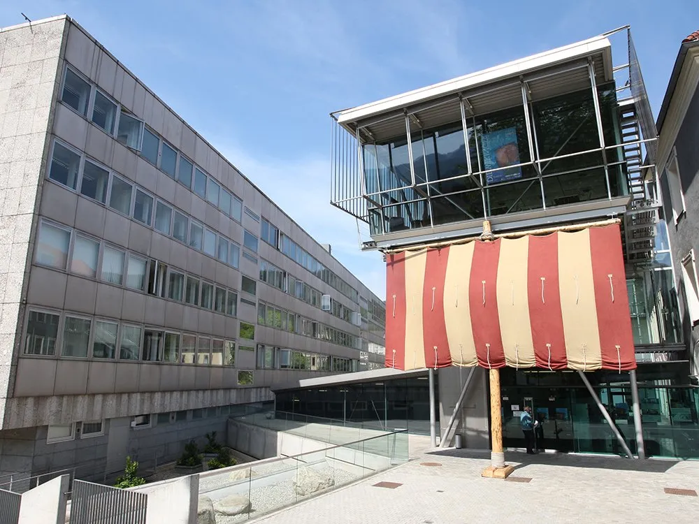 Außenansicht: Eingang Kunsthalle Leoben mit horizontal rot-weiß gestreiftem Segel