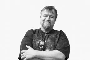 Halbporträt in schwarz-weiß: lächelnder Mann mit kurzem Haar und Bart, trägt dunkles Shirt und hat Arme verschränkt