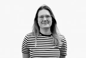 Halbporträt in schwarz-weiß: lächelnde Frau mit langen Haaren und Brille, trägt gestreiftes Oberteil 