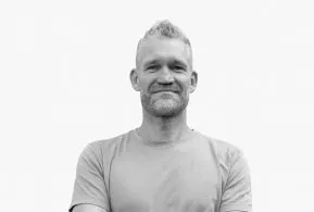 Halbporträt in schwarz-weiß: Mann mit kurzen Haaren und Bart, trägt helles Oberteil