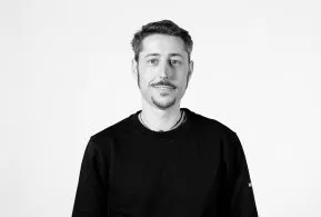 Halbporträt in schwarz-weiß: Mann mit kurzen Haaren und Bart, trägt dunkles Oberteil