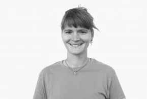 Halbporträt schwarz-weiß: Frau mit Stirnfransen und zurück gebundenen Haaren, trägt helles Shirt