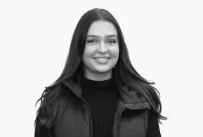 Halbporträt in schwarz-weiß: lächelnde Frau mit langen Haaren, trägt dunkles Oberteil und Jacke 