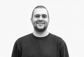 Halbporträt in schwarz-weiß: Mann mit kurzem Haar und Bart, trägt dunkles Oberteil