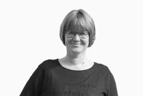 Halbporträt in schwarz-weiß: lächelnde Frau mit kurzem Haar und Brille, trägt dunkles Oberteil