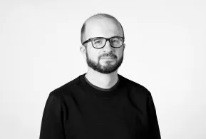 Halbporträt in schwarz-weiß: Mann mit Glatze und Brille, trägt dunkles Oberteil