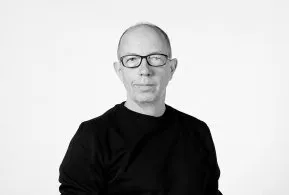 Halbporträt in schwarz-weiß: Mann mit Glatze und Brille, trägt dunkles Oberteil