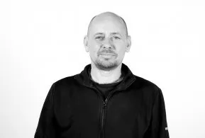 Halbporträt in schwarz-weiß: Mann mit Glatze und Bart, trägt dunkle Jacke