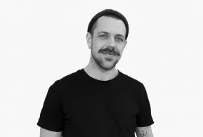 Halbporträt in schwarz-weiß: Mann mit Mütze und Bart, trägt dunkles Oberteil