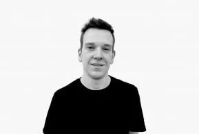 Halbporträt in schwarz-weiß: Mann mit kurzen Haaren, trägt dunkles Oberteil